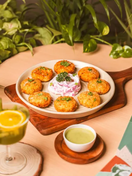 A plate of golden-brown appetizers served on a wooden board with fresh greens in the background. The bright, natural styling gives a fresh and healthy feel, suitable for cafes and casual dining.