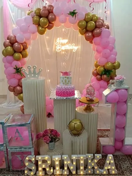 A pretty in pink first birthday setup. The circular balloon arch in shades of pink and gold, paired with transparent "BABY" blocks, creates a classic and adorable look.