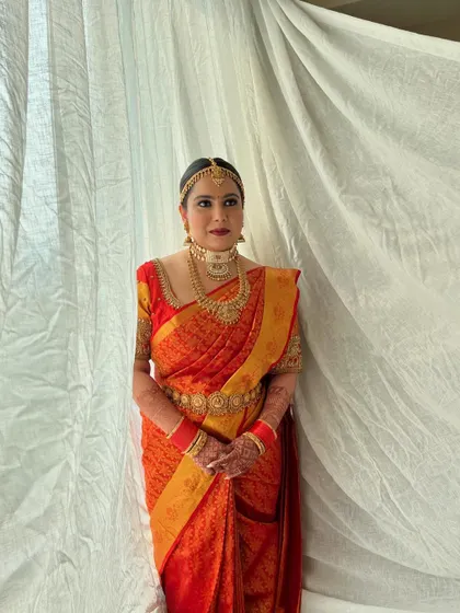 A full-length view of the bride in her stunning red and gold Kanjeevaram saree. The makeup is designed to balance the richness of her traditional attire.