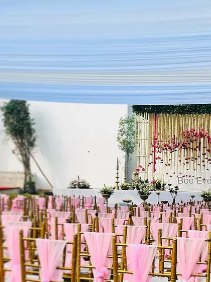 A beautiful outdoor wedding setup with pink-draped chairs leading to an elegant floral stage. The open-air setting and the soft color palette create a romantic and dreamy atmosphere.