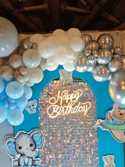 A cute baby elephant theme with a silver sequin arch backdrop, a 'Happy Birthday' neon sign, and adorable character cutouts.