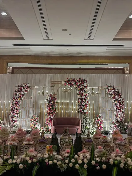 A contemporary stage with geometric gold arches adorned with red and pink flowers, set against a white curtain backdrop.