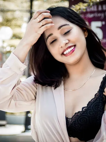 A joyful, candid outdoor shot. The model is laughing with her eyes closed, capturing a moment of pure happiness in a natural, sunlit environment.