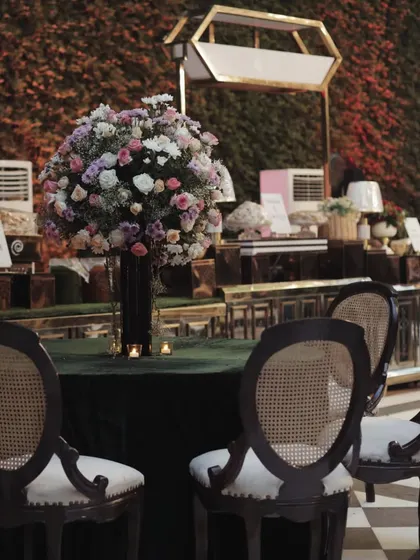 An elegant table setting for a cocktail event, featuring a large floral centerpiece and classic rattan-backed chairs.