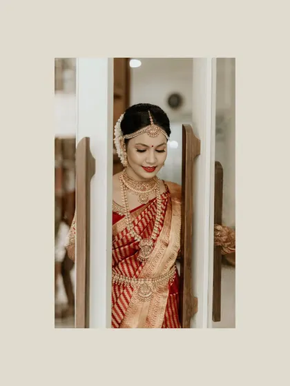 A beautiful South Indian bride, peeking through a doorway. Dressed in a traditional red and gold saree, her quiet anticipation is perfectly captured in this elegant frame.