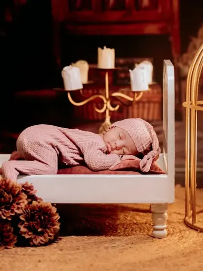 A warm and cozy newborn session with vintage-inspired props. The baby sleeps peacefully on a miniature bed next to a glowing candelabra.