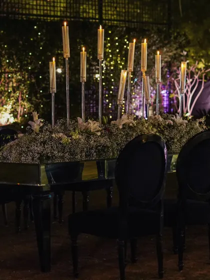 A long dining table set for an elegant outdoor meal, with tall candle arrangements providing soft, ambient lighting against the night sky.