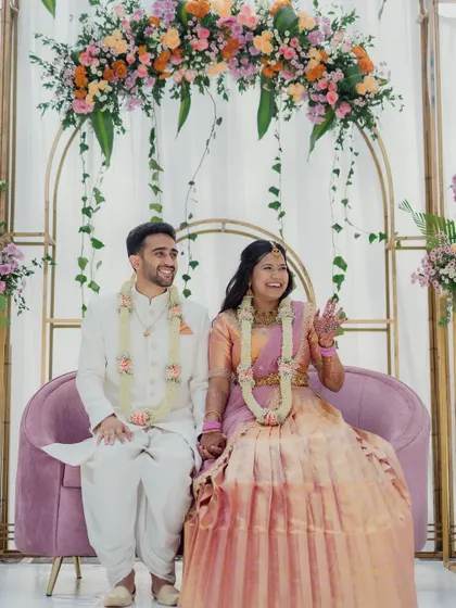 The happy couple enjoying their engagement ceremony on a chic stage, featuring a modern pink sofa and elegant golden arches adorned with flowers.