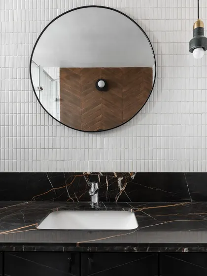 A modern bathroom design featuring a sleek black marble countertop with dramatic gold veining. We paired it with a simple round mirror and minimalist white tiles for a look that is clean and sophisticated.