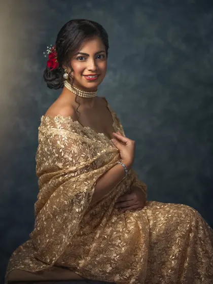 A woman in a stunning gold lace saree, with a red flower in her hair. This portrait exudes classic elegance and grace. The soft lighting and painterly background give it a timeless, celebratory feel.