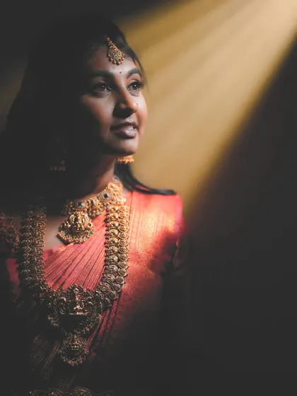 An artistic shot capturing the divine glow of this bride in her reception look. The traditional temple jewellery, with its warm antique gold finish, stands out beautifully against her pink saree.
