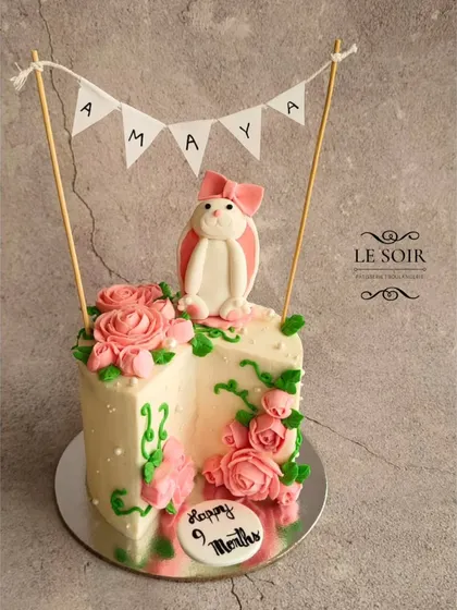 This three-quarters cake is a unique way to celebrate a nine-month milestone. The cake is decorated with lovely pink buttercream roses, a fondant bunny, and a cute "Amaya" banner.