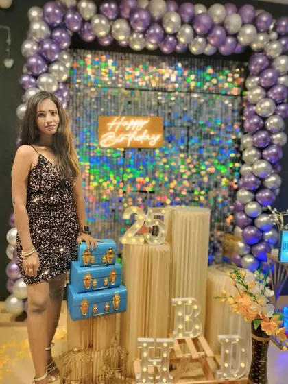 A full-length shot of a guest at her 25th birthday party. The decor, featuring a shimmer wall and purple balloons, creates a perfect photo-op.