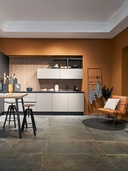 An earthy terracotta wall color provides a warm and inviting backdrop for this kitchen, which combines dark grey and light beige cabinets for a layered, modern look.