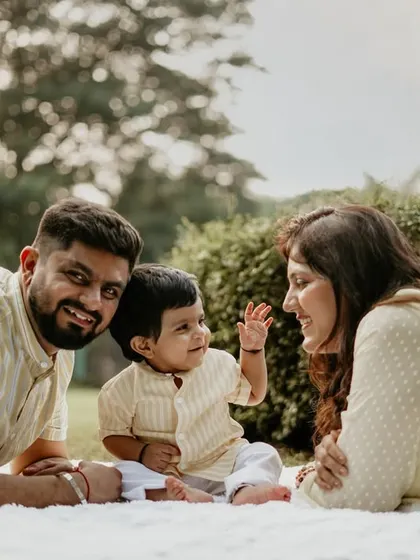 A relaxed family picnic scene, with the baby waving and interacting with his parents. This candid style captures the natural dynamic of the family.