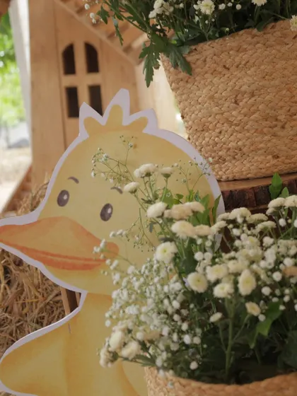 A cute duckling cutout peeks out from behind a floral arrangement, adding another sweet animal detail to the farm party theme.