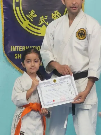 A young girl proudly holds her 7th Kyu (orange belt) certificate. Her focus and fist show the spirit of a true karateka.