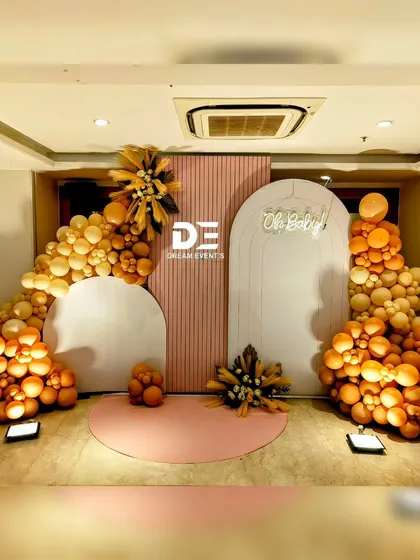 A sophisticated and modern baby shower setup using arched panels and a stunning boho-inspired balloon garland in shades of burnt orange and cream. The 'Oh Baby' neon sign adds the perfect finishing touch.