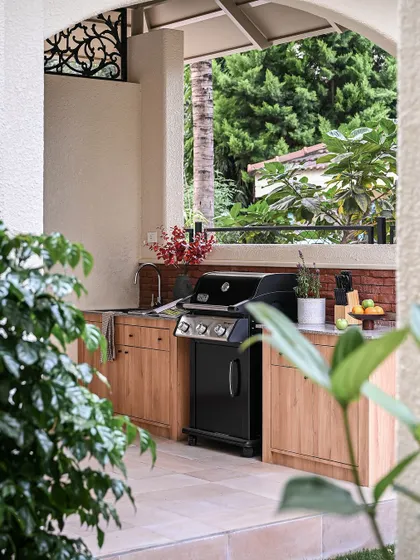 This is the outdoor kitchen I designed for the Modern Spanish Home, located in a covered arched gazebo. It's fully equipped for barbeque nights and features warm wood cabinetry and a durable granite countertop.
