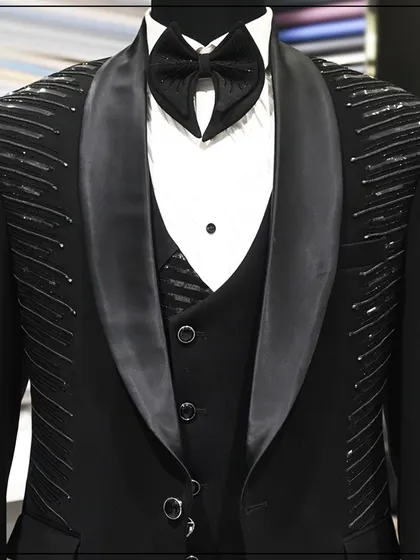 A full look at a black three-piece tuxedo with linear silver embroidery on the shoulders and lapels. The design is modern and architectural, perfect for a fashion-forward client.