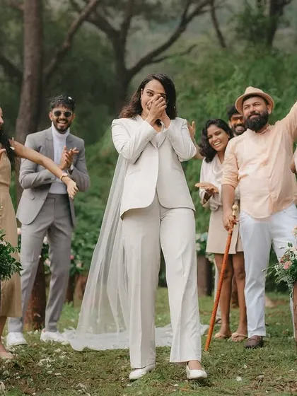 The bride, dressed in a chic white suit, walks down the aisle to the cheers of her loved ones. Her joyful, surprised expression is a beautiful, unscripted moment.