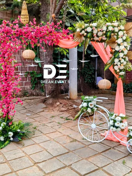 A whimsical and colorful entrance piece for an outdoor event. I combined a vibrant pink bougainvillea arch with a decorative white bicycle filled with flowers, creating a perfect photo spot and a cheerful welcome.