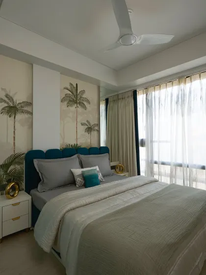 A full view of the tropical-themed guest bedroom, showcasing the bold wallpaper, layered bedding, and large window that fills the space with natural light.