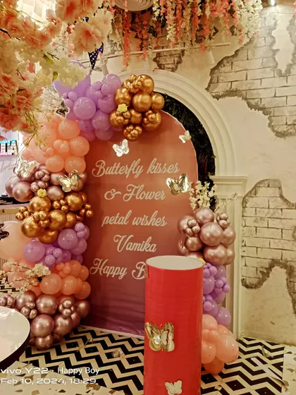 A butterfly-themed first birthday with a beautiful quote on the backdrop. The decoration uses a mix of pink, purple, and gold balloons, set against a rustic-chic venue.