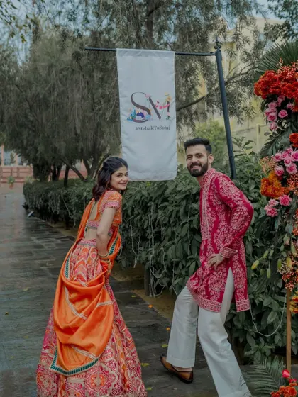 A fun moment with the couple posing next to their custom wedding signage and a vibrant floral arch.