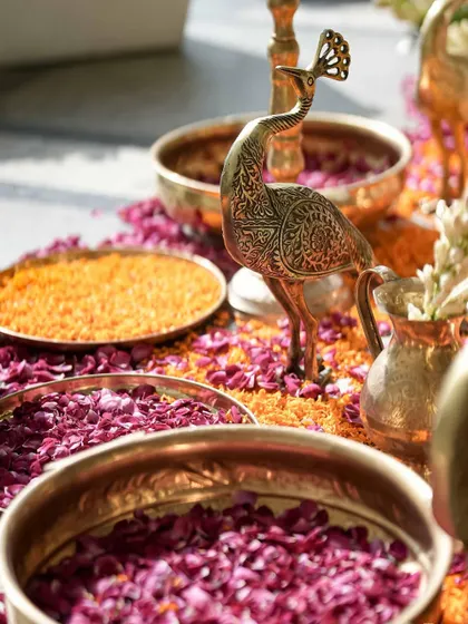 Details from our Kerala-inspired haldi, featuring brass peacock figurines and bowls of fresh marigold and rose petals.