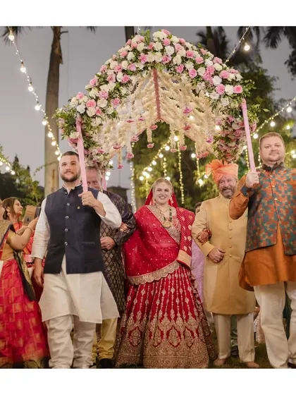 A bride's joyful entry under a 'phoolon ki chadar' held by her brothers. This image captures the family support and celebration during a cross-cultural wedding.