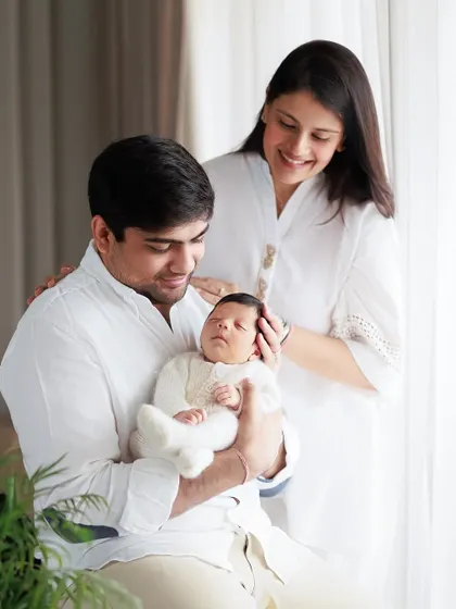 A beautiful family moment captured during a home session. The natural light from the window creates a soft and gentle atmosphere as they admire their newborn.