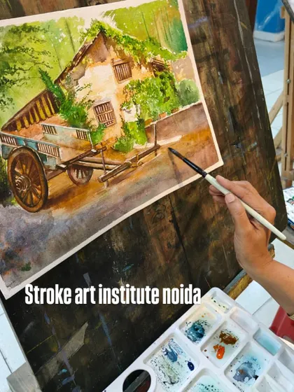 The artist's hand and palette are in focus here, showing the mixing of colors before they are applied to the rustic landscape painting.