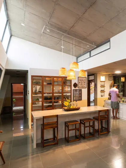 A duplicate of image 88, showing the kitchen at "Aamra." The space is designed for a food stylist, with an upcycled pantry, a large central island, and a cooking counter that looks out onto a large mango tree.
