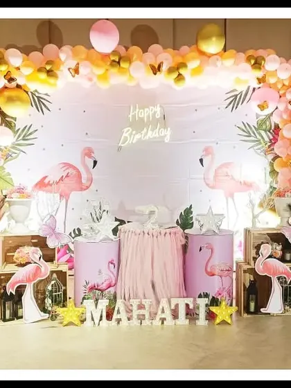 This flamingo-themed second birthday for Mahati is tropical and fun. The setup includes pink flamingo cutouts, a "Happy Birthday" backdrop, and a balloon arch in shades of pink, orange, and gold.