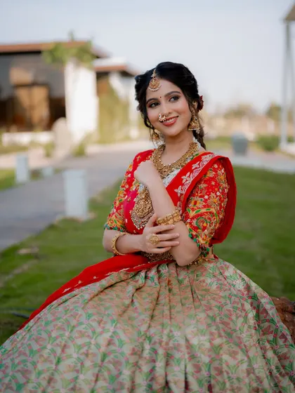 A joyful seated portrait. The composition allows the intricate patterns of the lehenga skirt and the heavy bridal jewelry to be the center of attention.