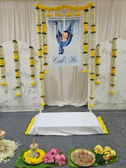 This is the full view of our Noolukettu stage decor. The design is centered around the "Call Me" banner for the name reveal, framed by beautiful flower garlands and flanked by modern arched panels for a touch of contemporary elegance.