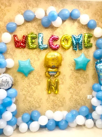 A "Welcome" home decoration for a new baby boy. The setup includes a blue and white balloon arch and a baby boy foil balloon.