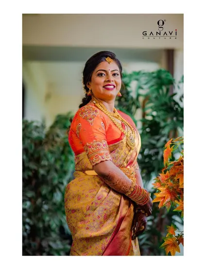 Bride Yamuna looking absolutely stunning in a custom orange blouse with scalloped, embroidered sleeves. Her joyful expression and vibrant attire make for a beautiful bridal portrait.