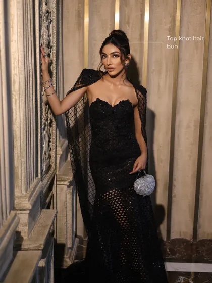 A full view of the look, showing how the sleek top knot bun complements the dramatic black gown and sophisticated makeup.