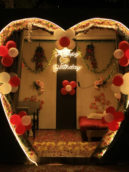 A heart-shaped cabana decorated for a romantic birthday celebration. The setup includes custom lighting, balloons, and a comfortable seating arrangement.