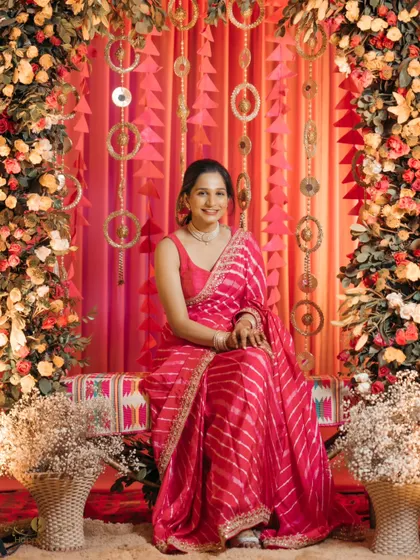 A lovely portrait of the bride seated against a colorful and festive backdrop at her mehndi ceremony. Her bright pink saree and happy smile are radiant.