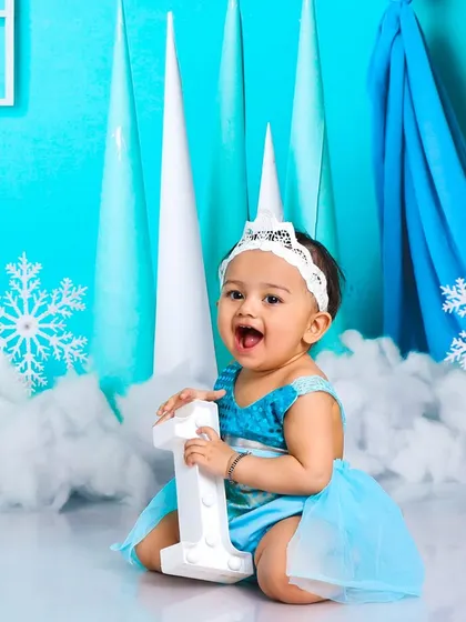 Celebrating her first birthday like royalty. This little princess is holding her "One" sign, surrounded by a magical snowy landscape.