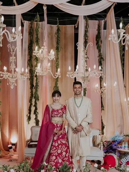 An elegant reception stage featuring blush pink drapes, hanging greenery, and crystal chandeliers, creating a sophisticated and romantic atmosphere for the couple.