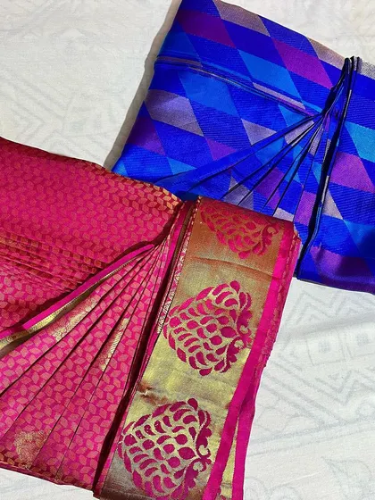 A vibrant duo of a pink Banarasi and a geometric blue silk saree. Both are pleated and folded, ready for two different occasions.