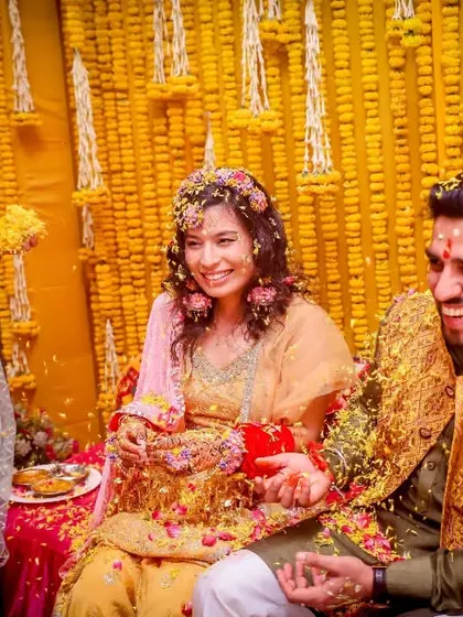 The colourful version of a joyous Haldi moment. The bright yellow marigold flowers and the couple's happy faces create a vibrant and energetic photograph.
