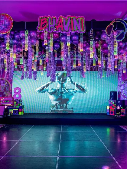 A full view of the neon party stage, featuring a DJ booth, multiple boombox props, and a large LED screen with futuristic graphics.