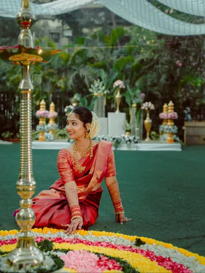 A serene portrait of a South Indian bride seated by a traditional lamp and floral rangoli.