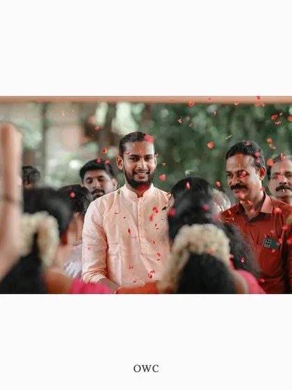 A candid shot of the groom being showered with flower petals as he enters the wedding venue.