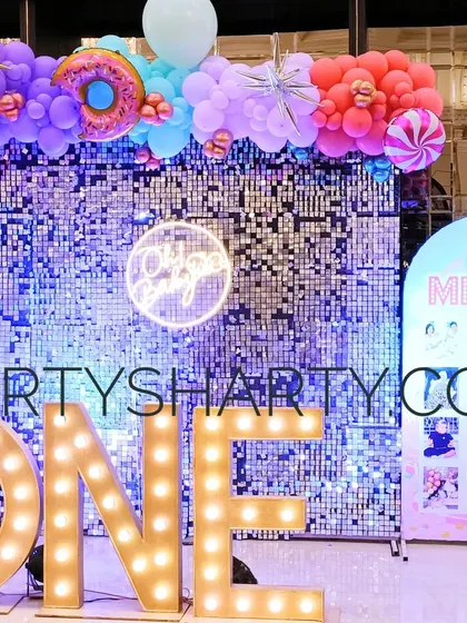 A 'ONE' marquee sign against a silver sequin wall, perfect for a first birthday celebration with a glamorous candy theme.